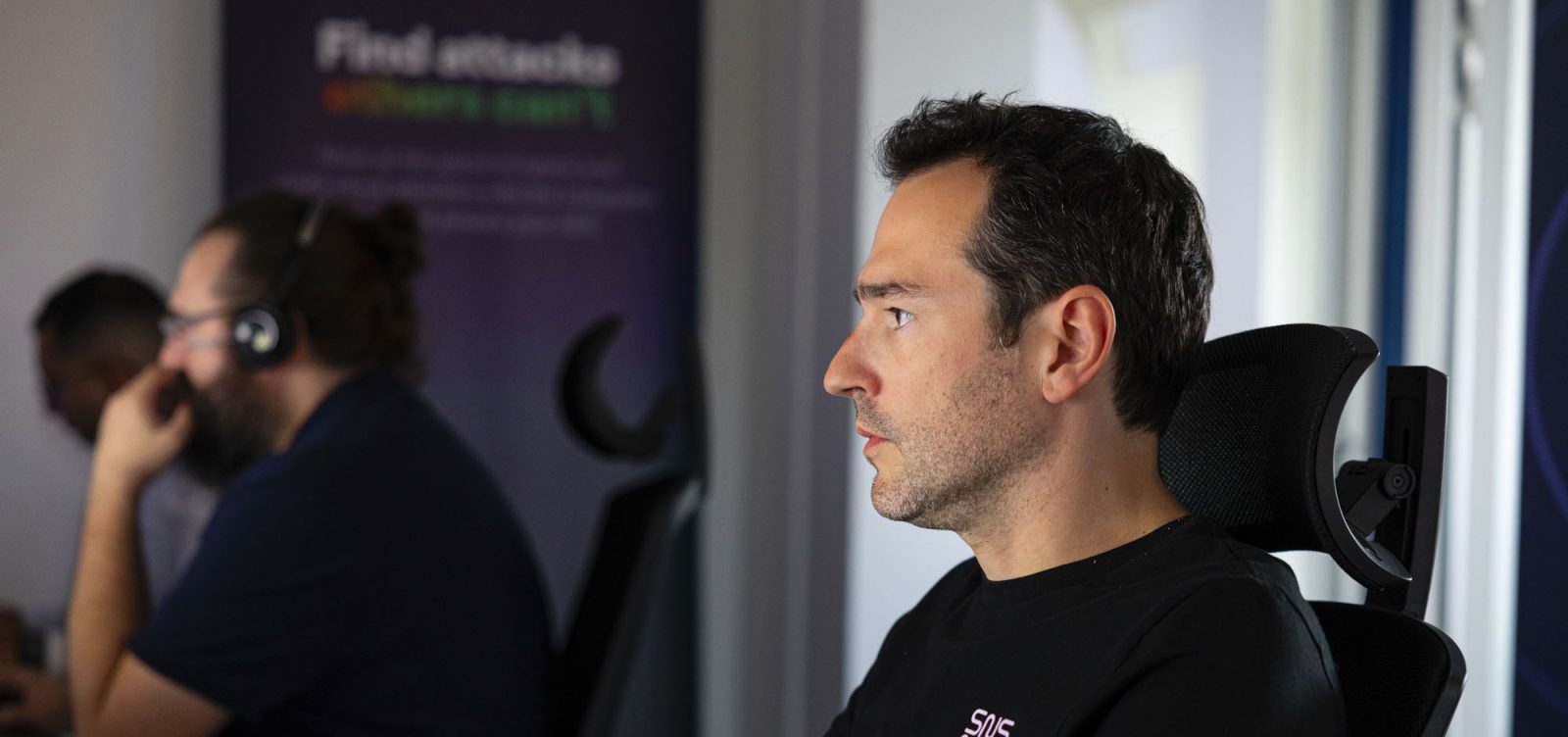 analyste SOC portant un t-shirt noir SNS Security à son poste de travail