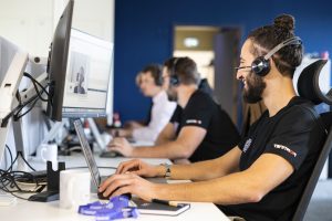 ingénieur support avec un casque qui sourit assis à son poste de travail à côté d'autres ingénieurs