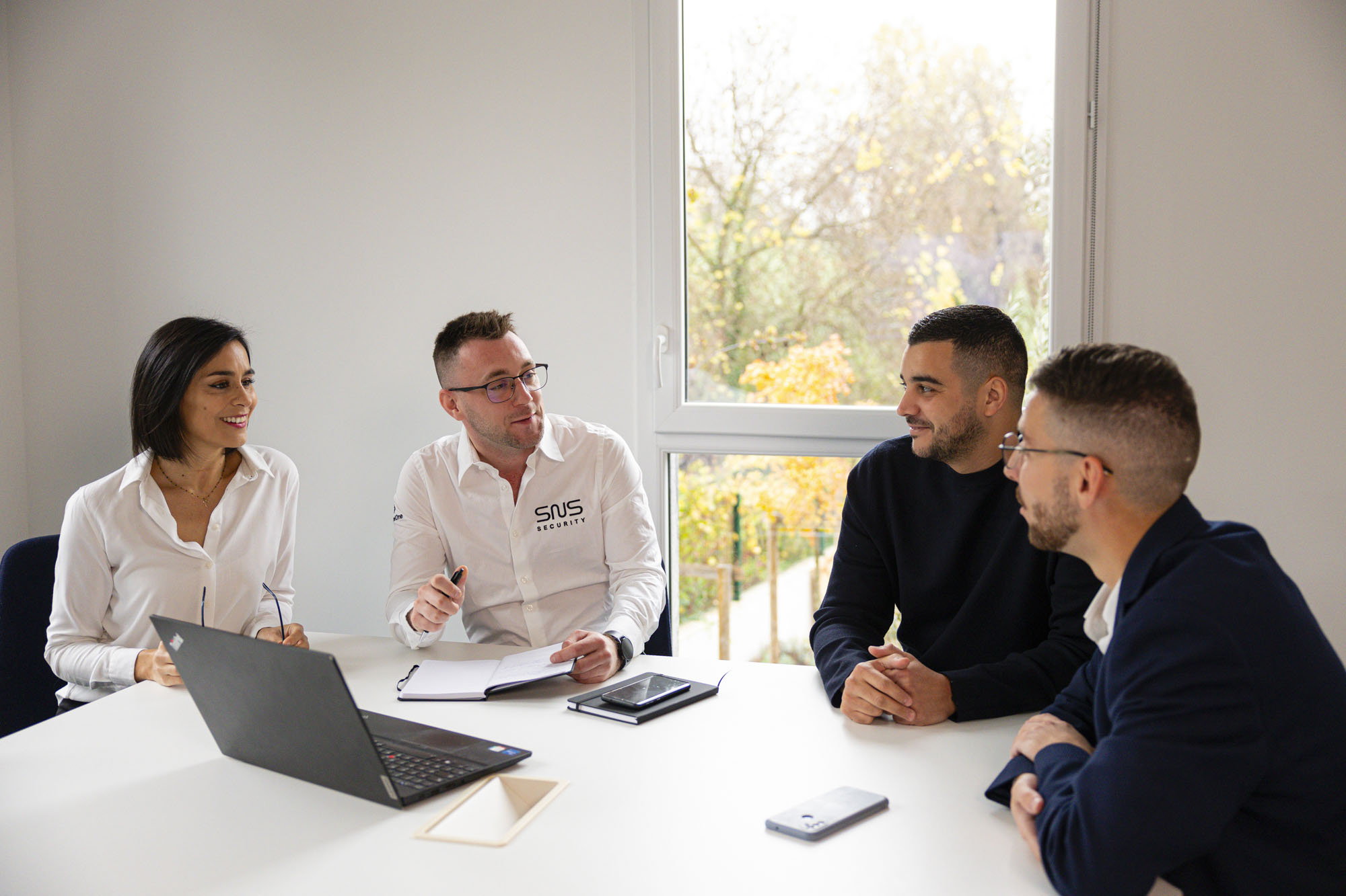 deux collaborateurs SNS Security assis autour d'une table de réunion avec deux clients